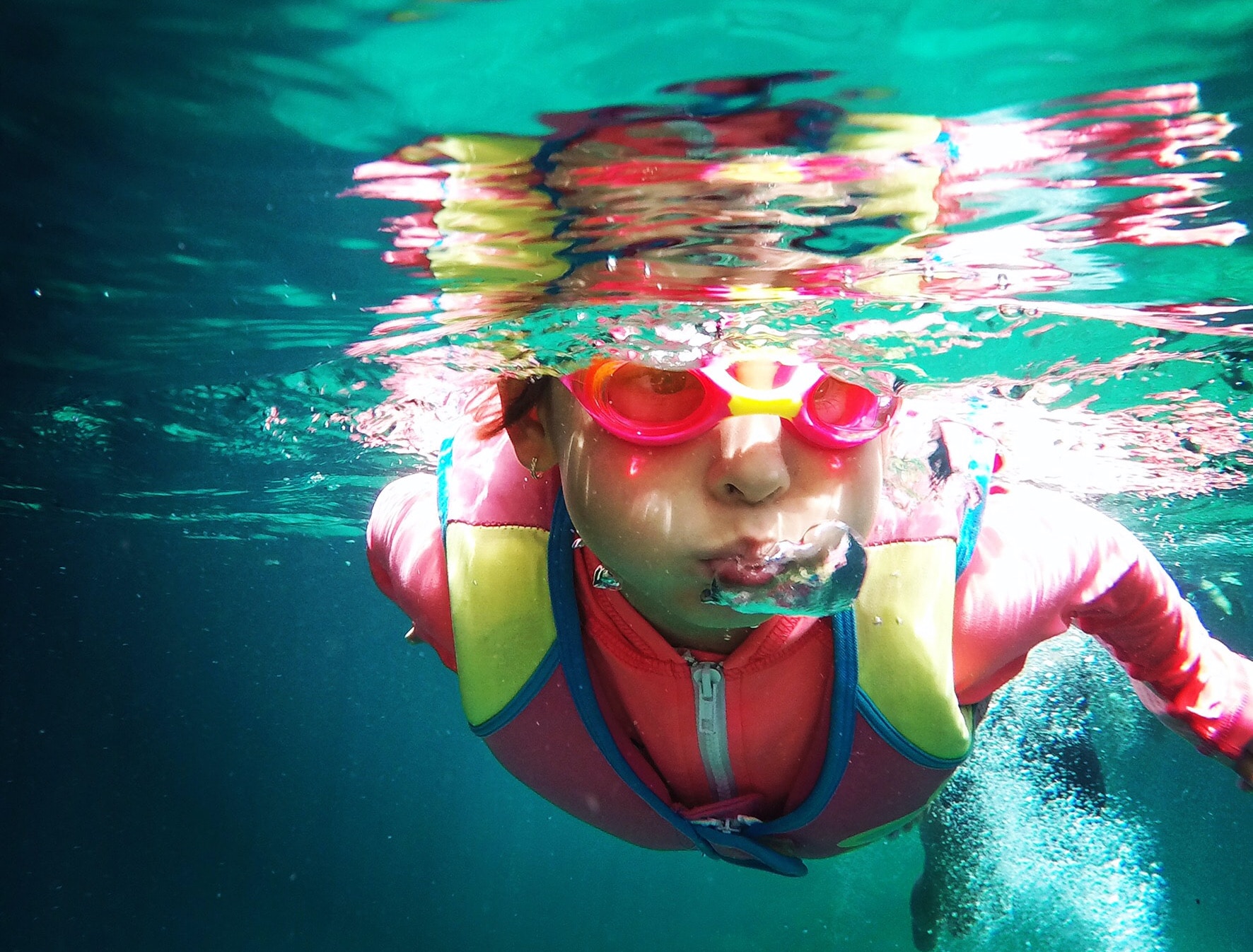 child swimming in pool with goggles and life vest